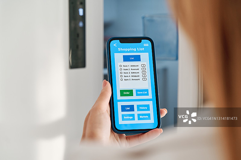 女人在智能家居中使用智能手机上的应用程序制作购物清单图片素材