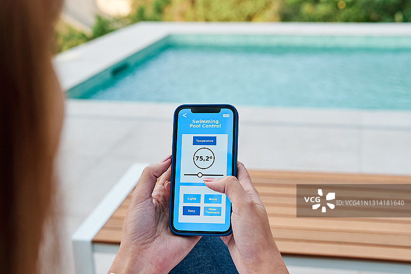 女人使用智能手机上的应用程序来控制游泳池的水温图片素材
