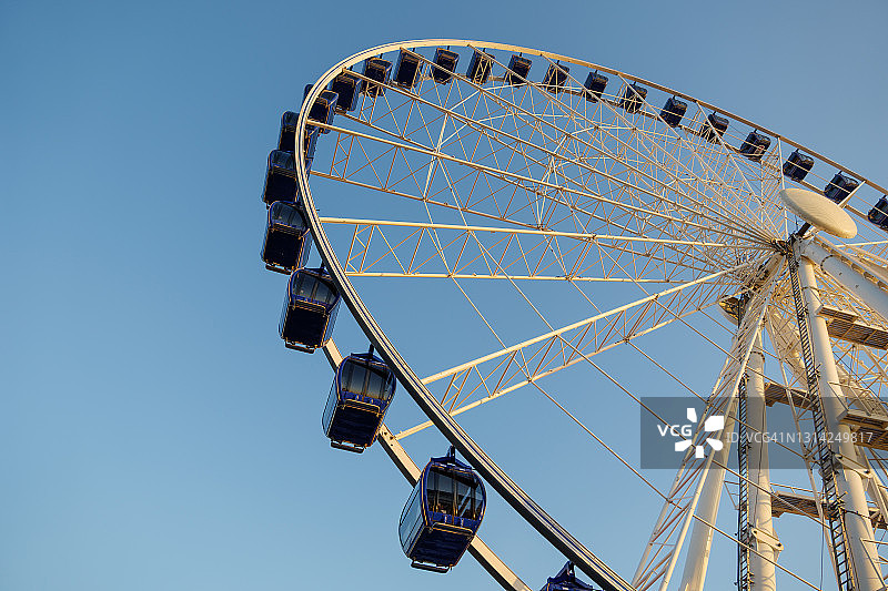 晴朗蓝天下，摩天轮白色结构和蓝色舱体的仰视角度图片素材
