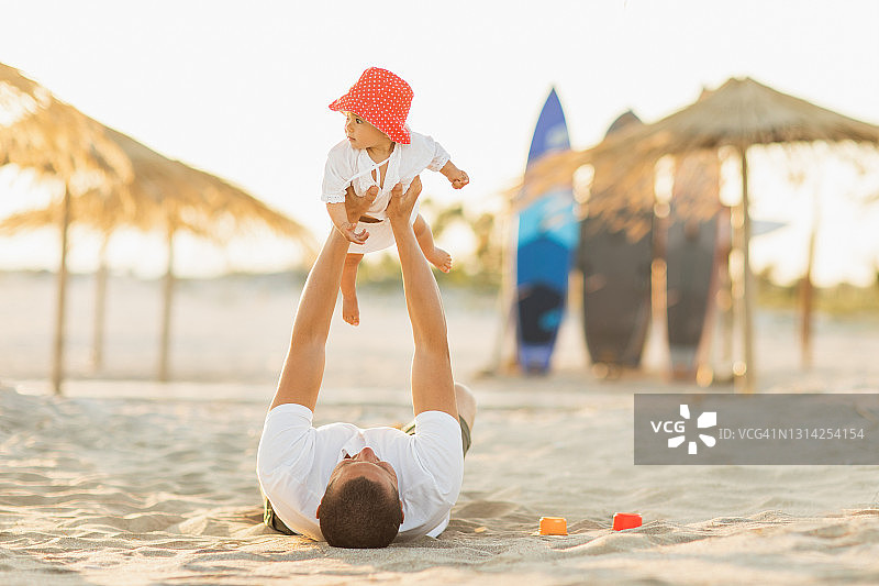在金色时刻，男人和婴儿在美丽的海滩上玩沙子图片素材