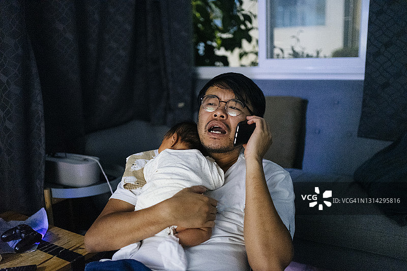 亚洲单身父亲使用手机，担心新生女儿睡不着图片素材