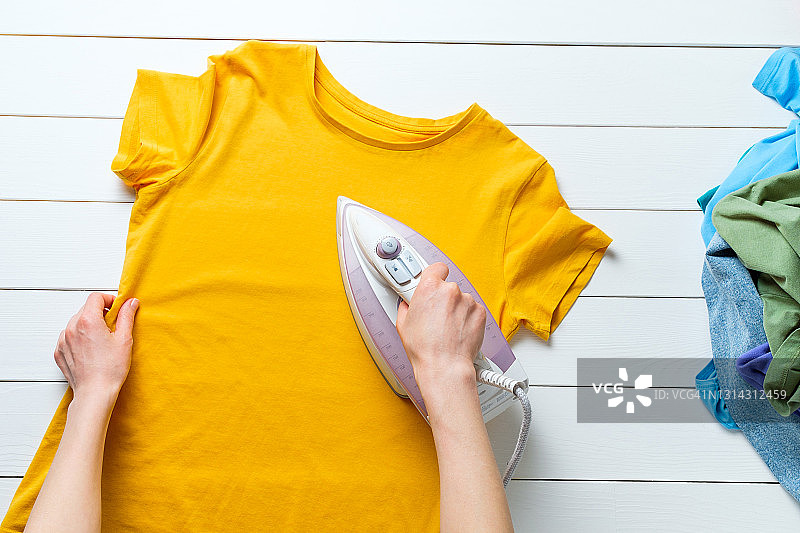 散落的明亮干净的彩色衣服抽象背景，一个女人正在熨烫T恤，家庭作业和责任的概念，缺乏做家务的时间图片素材