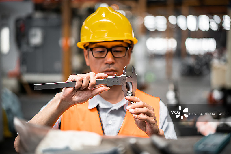 亚洲男性蓝领工人在工厂测量零件图片素材