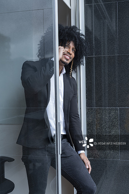 在办公室里穿着正装，在办公室窗户旁查看手机与客户交谈的非洲裔卷发拉丁主管图片素材
