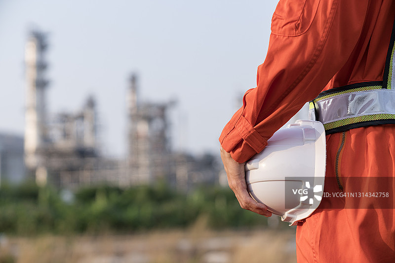 身穿西装，手持白色安全帽的工程师背影，背景为炼油厂图片素材