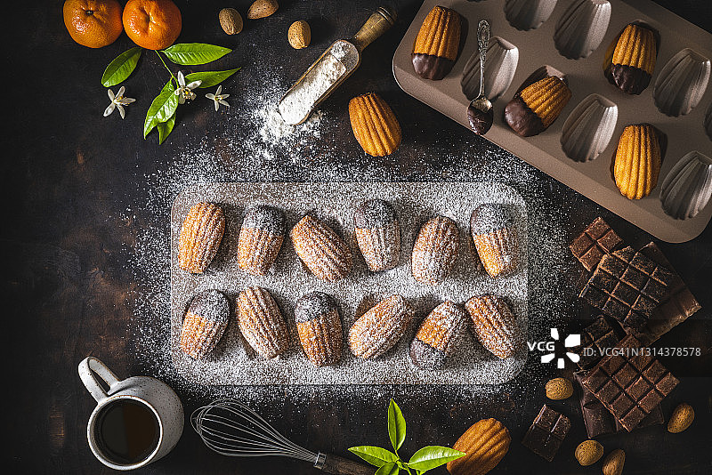 自制玛德琳，模具中融化的巧克力，撒上糖粉，深色木纹背景图片素材