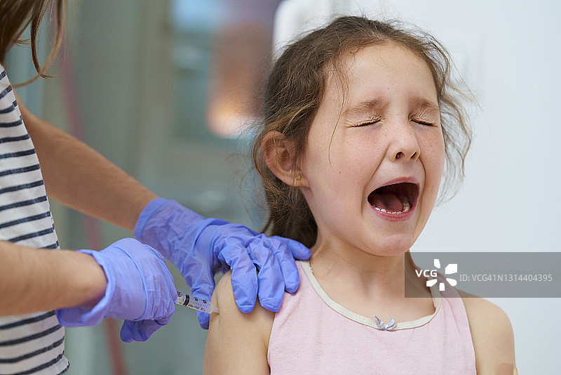 女孩戴蓝色医用手套为朋友接种疫苗，模拟新冠疫苗。医疗概念图片素材