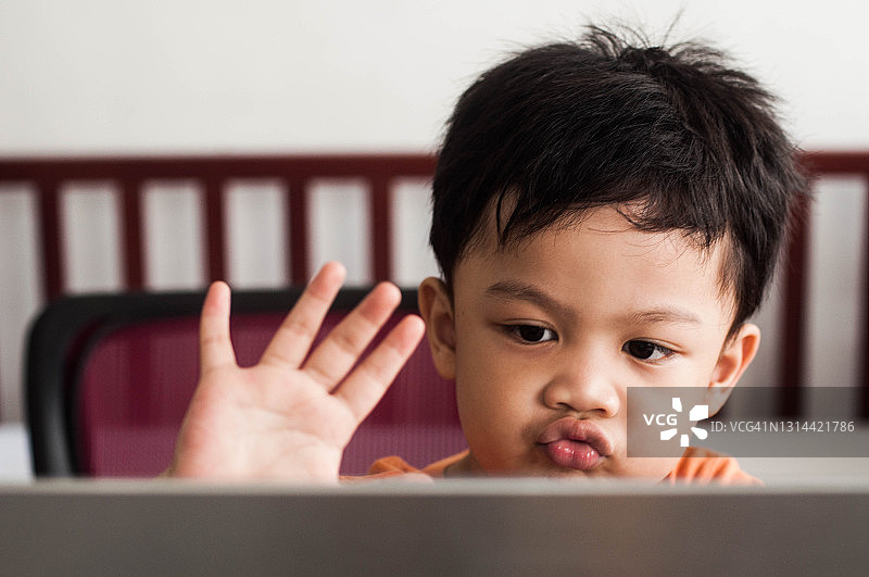 疫情期间，一名东南亚男童在家使用笔记本电脑进行在线学习图片素材