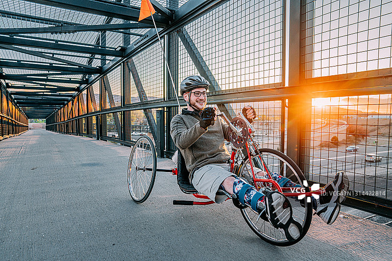 年轻男人，骑红色手摇车，城市日落人行天桥图片素材