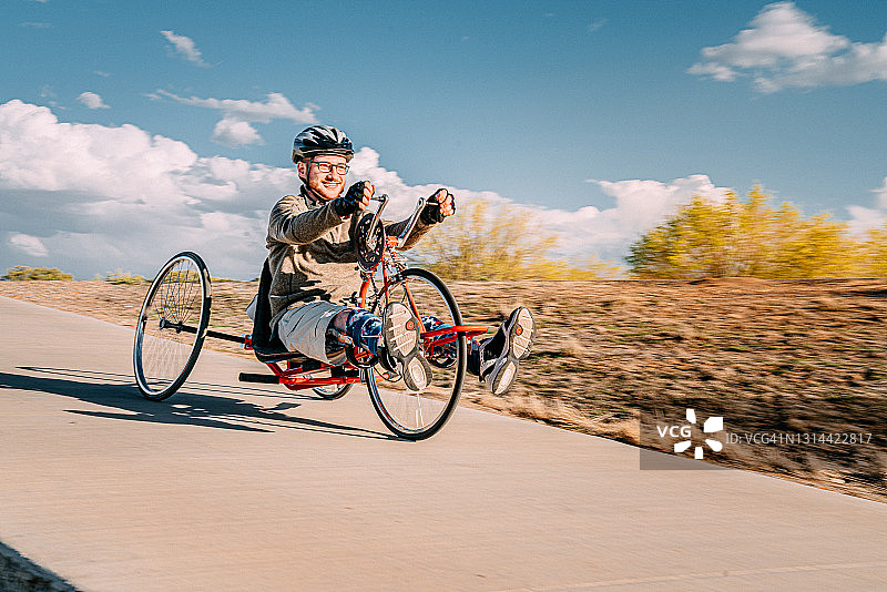 英俊的年轻男子在春天户外骑红色手摇车下坡，佩戴矫形腿部支架进行适应性锻炼图片素材