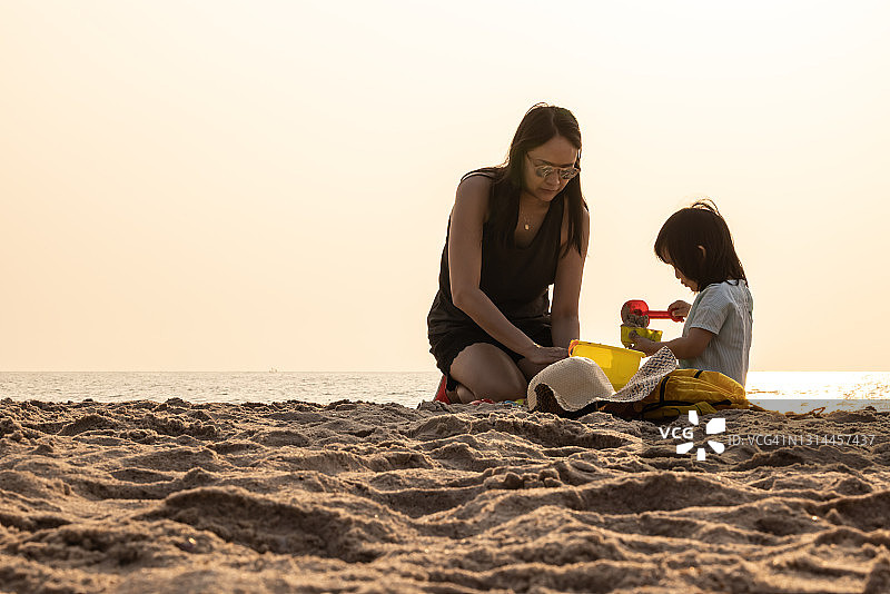 早晨，母亲和亚洲孩子在沙滩上玩沙子图片素材