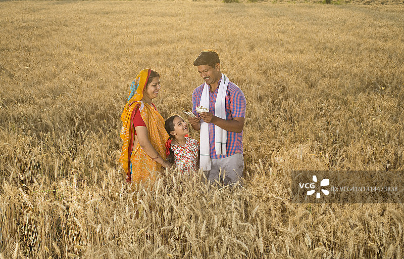 一家人在田野里，男人拿着印度卢比图片素材
