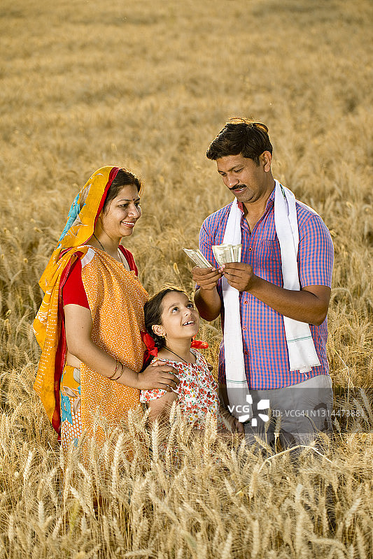 一家人在田野里，男人拿着印度卢比图片素材