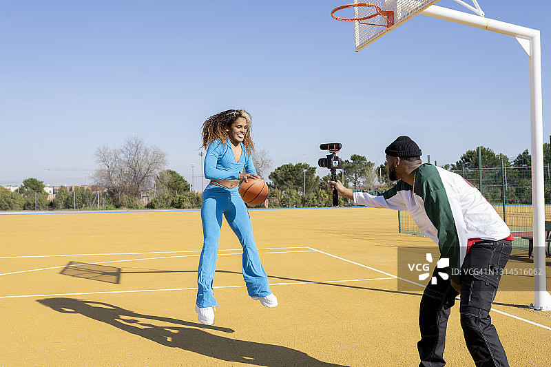 快乐的男女在运动场上用篮球进行视频博客图片素材