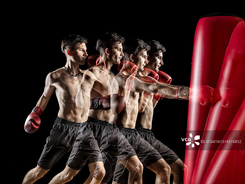 年轻的男拳击手在黑色背景下击打红色沙袋图片素材