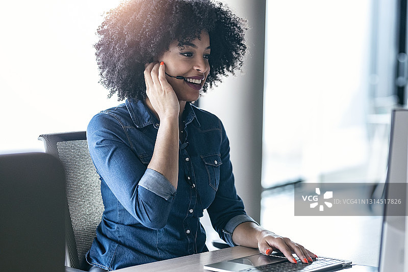 微笑的女客服代表在办公室的办公桌前戴着耳机通话图片素材