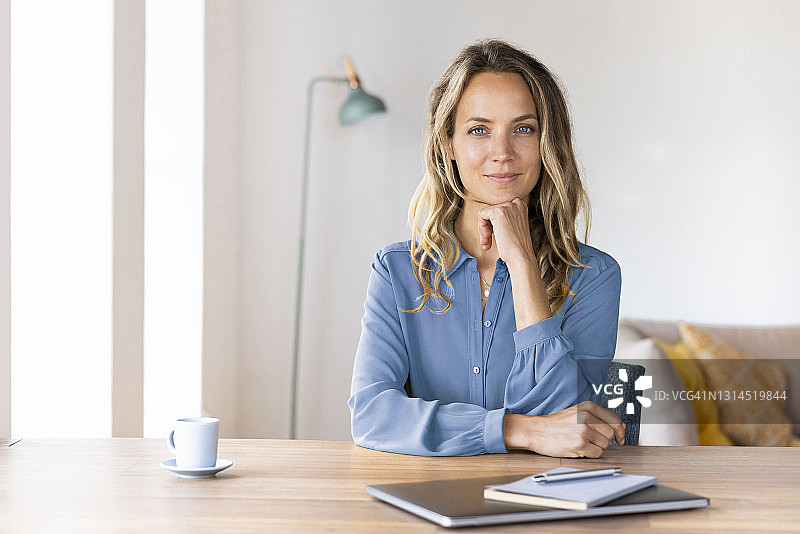 漂亮的女商人手托着下巴坐在家庭办公室的桌子旁图片素材