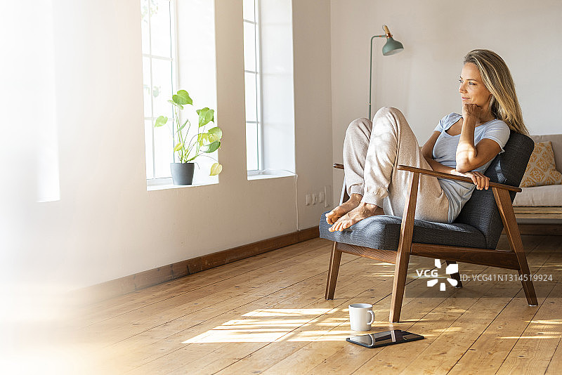 微笑的女人手托下巴坐在家里的椅子上图片素材