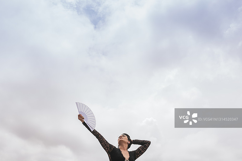 女舞者在多云的天空下，手持扇子表演弗拉门戈舞图片素材