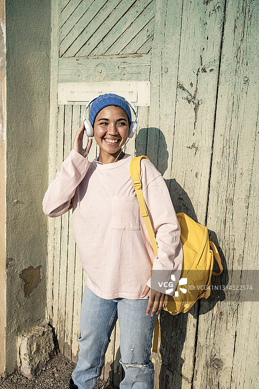 在阳光明媚的日子里，微笑的女人望着别处，戴着耳机听音乐图片素材