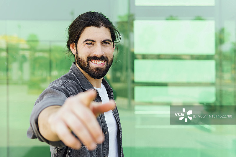 站在玻璃墙前做手势的微笑年轻人图片素材