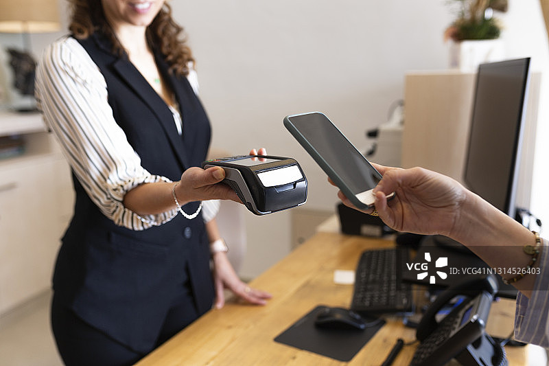 在酒店前台用手机连接信用卡阅读器的女商人图片素材