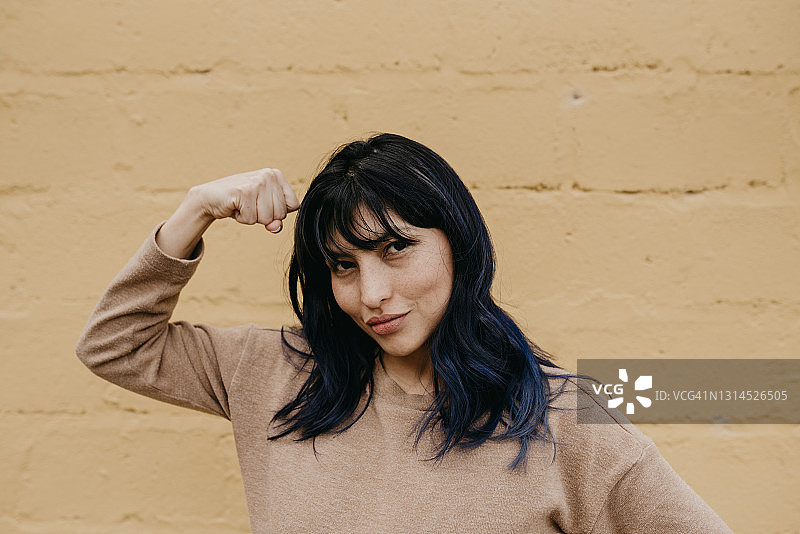 美丽的女人在墙前展示肌肉图片素材