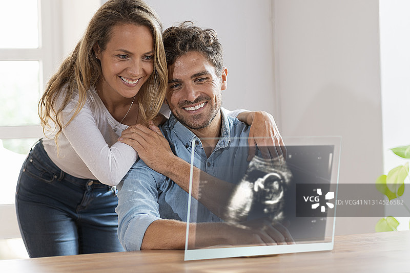 在家中隔着透明屏幕看超声波图像的恩爱夫妻图片素材