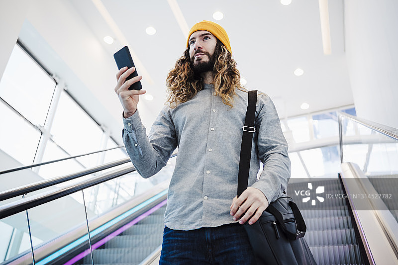 在自动扶梯上使用手机的留长发男子图片素材