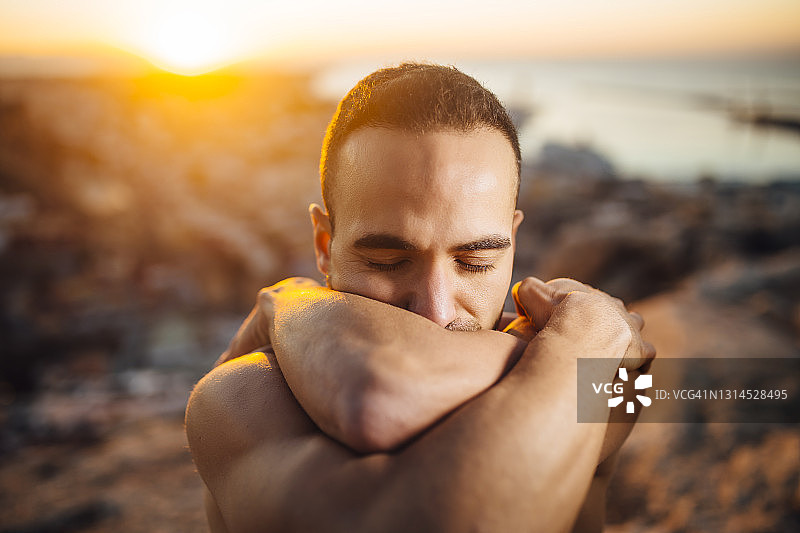 日出时分，闭着眼睛拥抱自己的赤膊男人图片素材