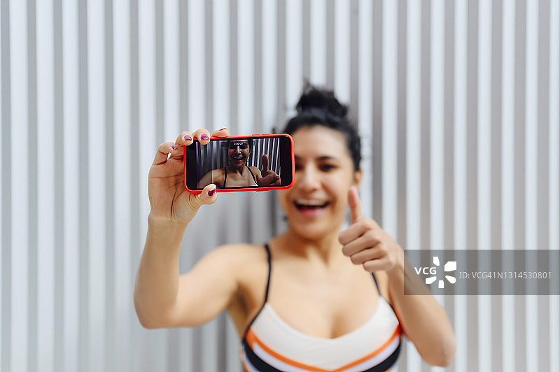 女运动员在墙前用智能手机拍摄图片素材