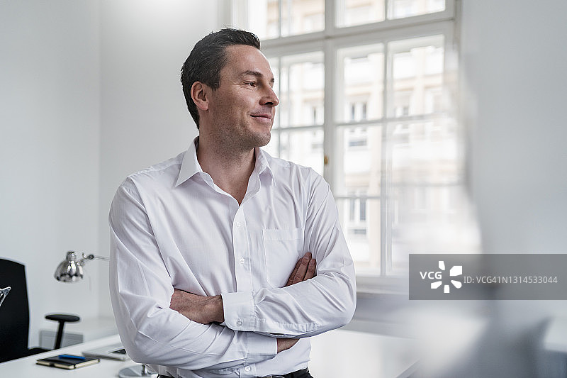 在办公室里双臂交叉望向远方的商人图片素材