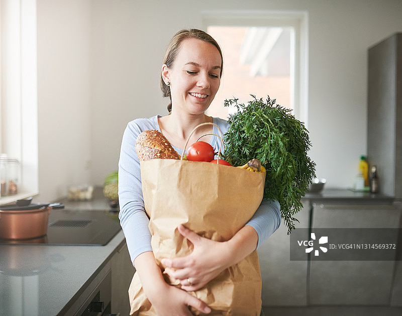 年轻女子在家中厨房从纸袋里取出新鲜农产品的肖像图片素材