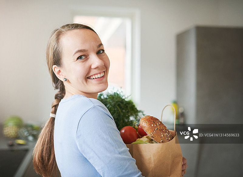 年轻女子在家中厨房从纸袋里取出新鲜农产品的肖像图片素材