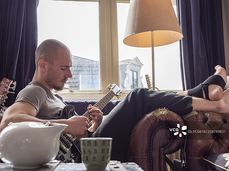 年轻男人在家中客厅弹吉他的局部照片图片素材