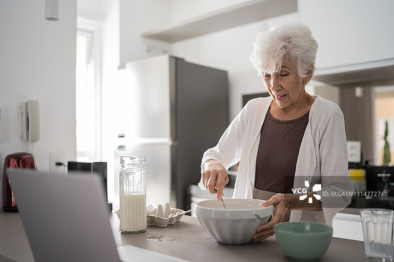 年长的女人在家使用笔记本电脑做饭图片素材