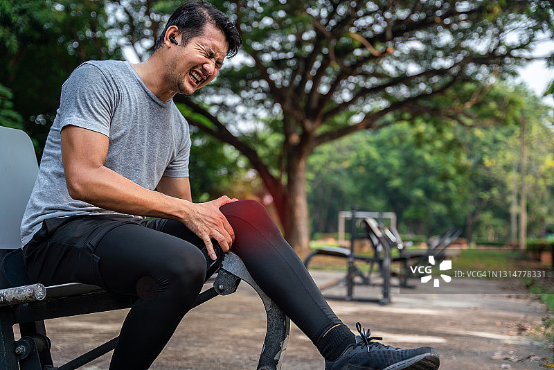 亚洲男性跑步者弯腰抱住膝盖，在公园锻炼时因急性膝盖损伤而感到剧烈疼痛，运动员膝盖受伤。特写。病变以红色突出显示。图片素材