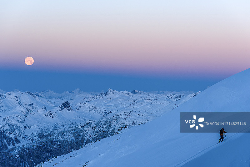 滑雪登山者在满月下攀登白雪皑皑的山坡图片素材