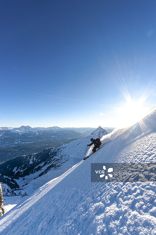 日出时分，滑雪登山者滑下陡峭的山脊图片素材