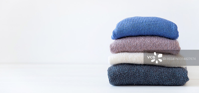 堆叠在白色木桌上的不同颜色的针织羊毛物品，冬季和秋季慈善保暖舒适毛衣，手工产品的存储、护理和洗涤理念，文本空间副本图片素材