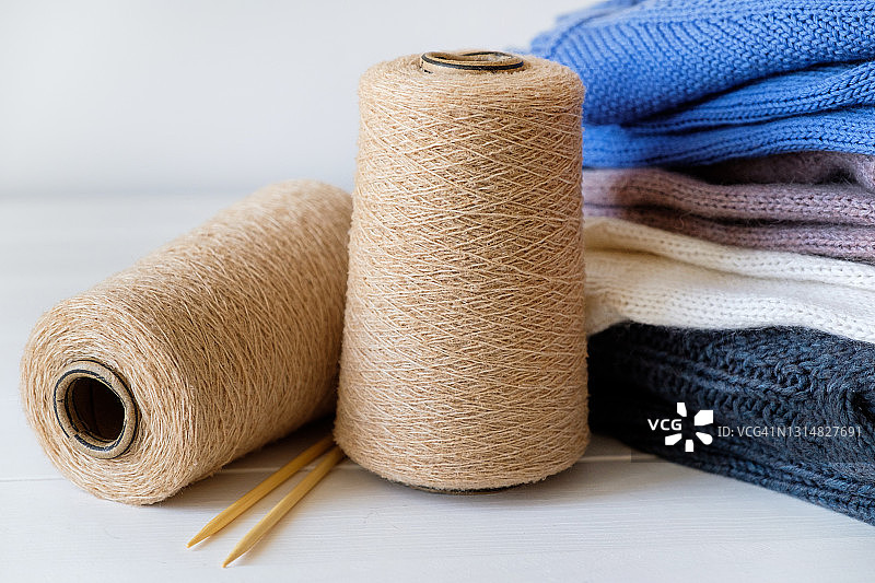 不同颜色的针织品堆放在一起，放在白色背景上。冬季和秋季保暖毛衣。旁边是毛线纱线和针织针的线团和线轴。爱好、存储、护理和洗涤手工制品的概念。图片素材