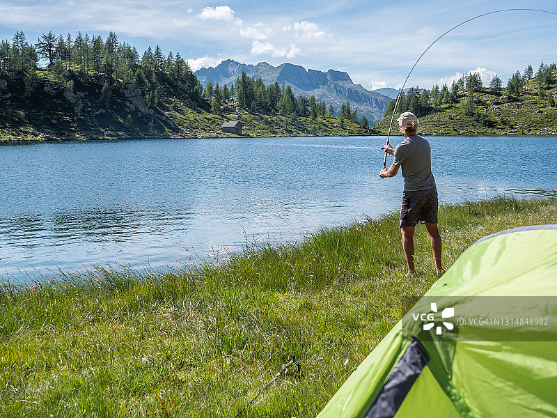 男子夏季在高山湖泊钓鱼和露营图片素材