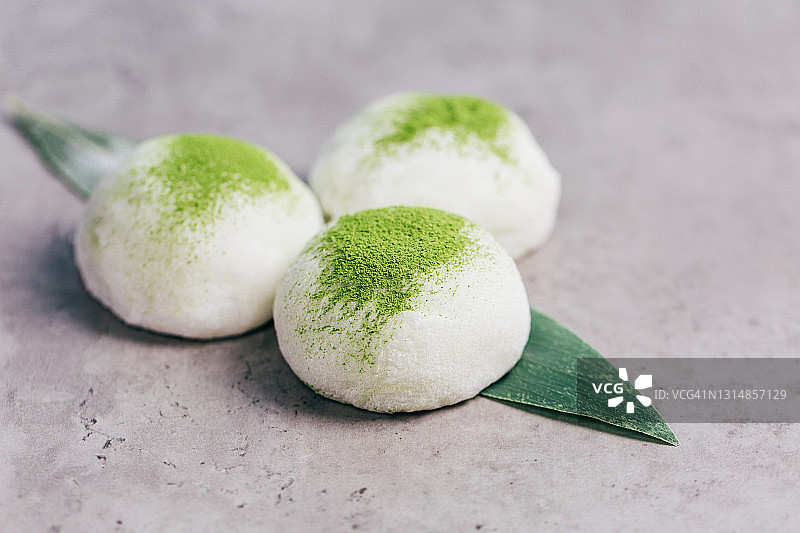 在混凝土纹理背景上的三个抹茶粉麻糬甜点。传统日式蛋糕。正面图图片素材