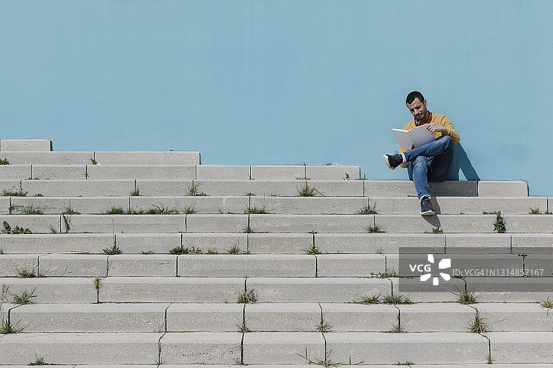 男人坐在户外楼梯上读书图片素材