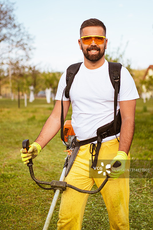 男子用汽油修剪机修剪浓密的草图片素材