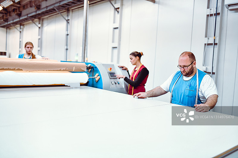 工厂工人在辊筒印花机上拉伸材料图片素材