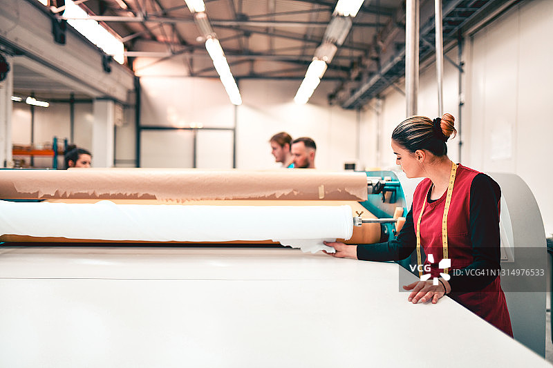 女纺织工人和同事一起检查辊筒机上的材料印花图片素材