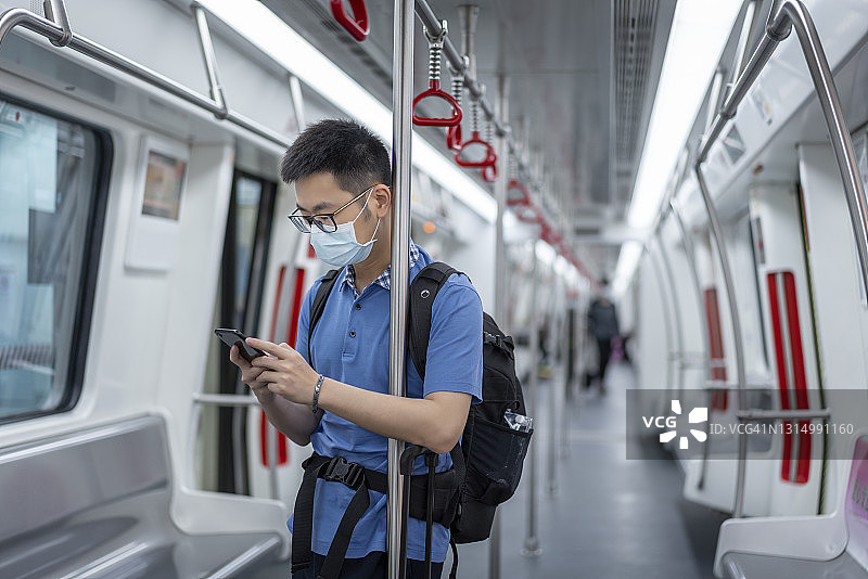 戴口罩用智能手机乘坐地铁的亚洲男人图片素材