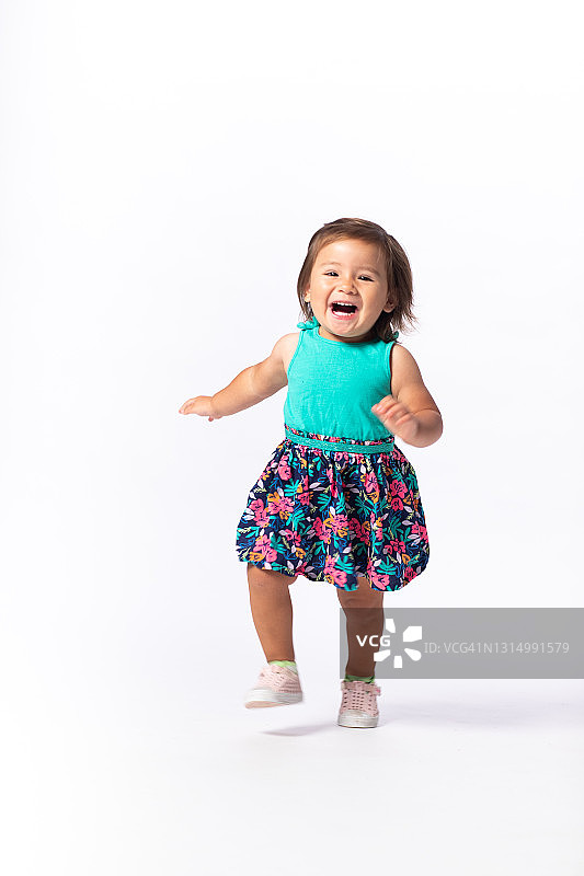 穿着蓝绿色上衣和碎花裙的女童兴奋地奔跑图片素材