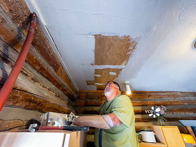 在墨西哥一所小房子里，残疾的干墙承包商使用假肢钩子修补天花板图片素材